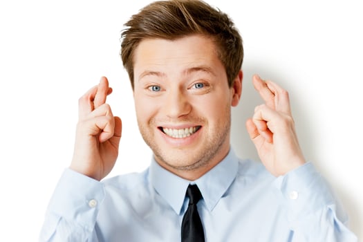 Waiting for a special moment. Happy young man in shirt and tie keeping fingers crossed and smiling while standing isolated on white photo