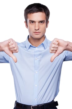 Rejected Serious young man in blue shirt showing his thumbs down and looking at camera while standing isolated on white photo