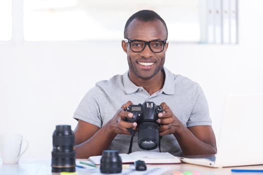 Successful journalist. Handsome young African man in casual wear sitting at his working place and holding camera photo