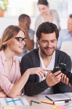 Discussing shots. Two co-workers holding camera and smiling while three people working on background photo