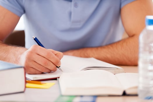 Studying hard. Cropped image of student writing something in note pad while sitting at the desk photo