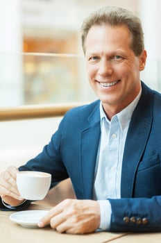 Having a break with fresh coffee. Cheerful mature man in formalwear drinking coffee and smiling while sitting in coffee shop photo