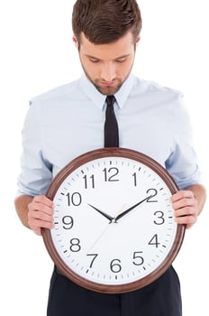 Checking the time. Handsome young man in shirt and tie holding a clock in his hands and looking at it while standing isolated on white background photo