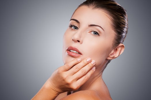 Forever young. Side view of shirtless mature woman looking at camera and touching her face with hand while standing against grey background photo