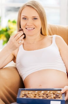 Eating chocolate candies. Beautiful pregnant woman sitting on the chair and eating chocolate candies photo