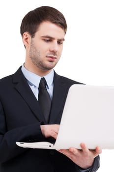 Working on laptop. Confident young man in formalwear working on laptop while standing isolated on white photo