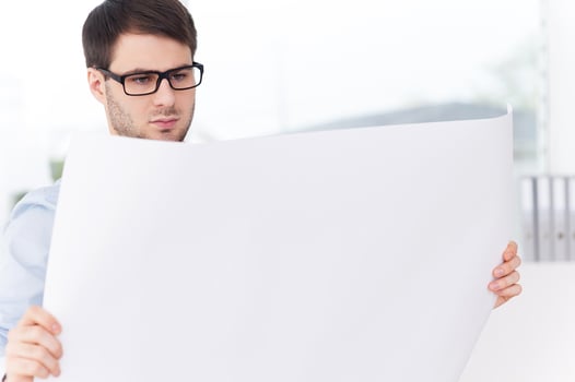 Architect with blueprint. Confident young man in shirt and tie examining blueprint while standing against the window photo
