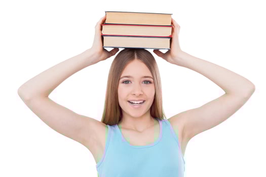 Smart schoolgirl. Cheerful teenage girl holding book stack on her head and smiling while standing isolated on white photo