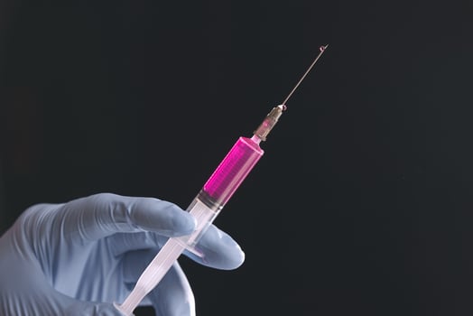 Doctor's blue-gloved hand holding a syringe with red liquid isolated on a black background. photo