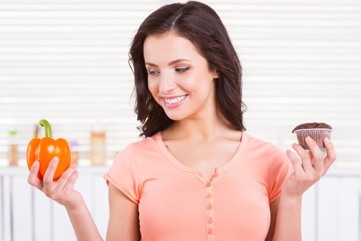 I choose healthy food. Cheerful young woman choosing what to eat while holding chocolate muffin and fresh pepper photo