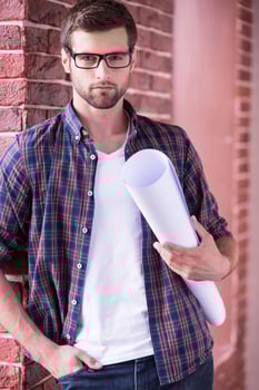 Architect with blueprint. Confident young man in glasses holding blueprint and looking at camera while standing indoors photo