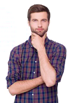 Generating new ideas for you. Thoughtful young man in casual shirt holding hand on chin and looking at camera while standing isolated on white photo
