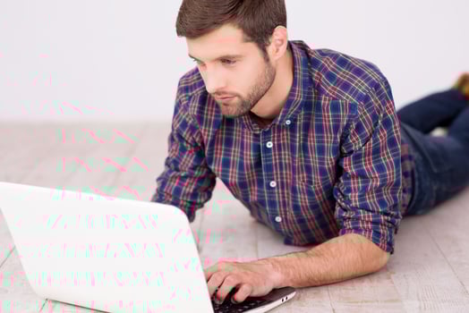 Man surfing the net. Handsome young man working on laptop while lying on hardwood floor photo