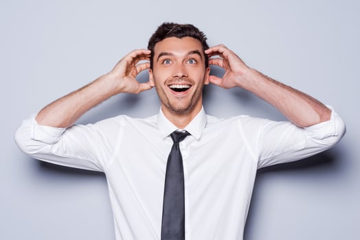 It is just unbelievable Happy young man in shirt and tie touching head with hands and smiling while standing against grey background photo