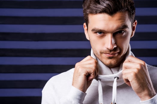 Stylish handsome. Handsome young man in white sweater adjusting his collar and looking at camera while standing against striped background photo