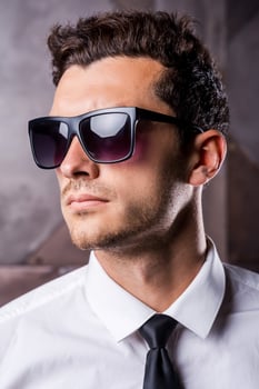 Always trendy. Confident young man in formalwear and sunglasses looking away while standing against metal background photo