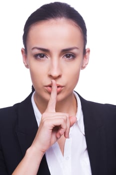 Keep silence Confident young woman in formalwear looking at camera and holding finger on lips while standing isolated on white background photo
