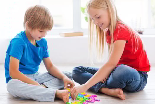 Kids playing at home. Two cute little children playing with plastic colorful letters while sitting on the hardwood floor photo
