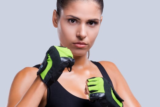 Defending herself. Attractive young sporty woman in sports gloves posing against grey background photo