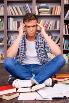 Trying to concentrate on studying. Frustrated young man touching his head with hands and keeping eyes closed while sitting against bookshelf photo