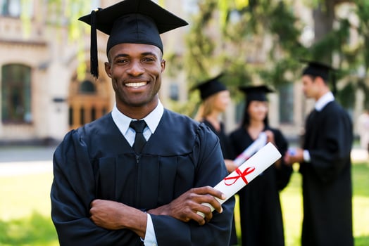 Happy graduate. Happy African man in graduation gowns holding diploma and smiling while his friends standing in the background photo