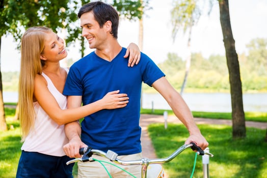 Spending great time together. Beautiful young smiling couple looking at each other and smiling while man leaning at bicycle in park photo