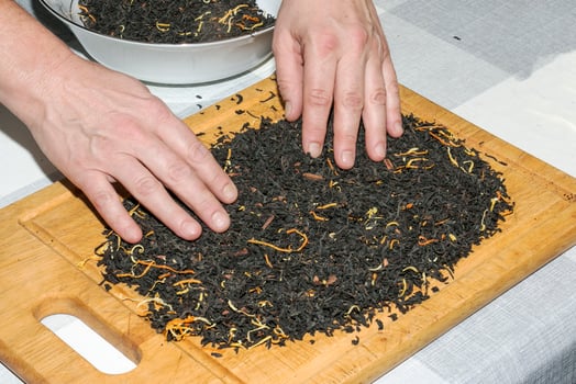 Female hands pour the tea mixture onto a wooden board to dry. The process of making a tea mixture from black tea, lemon and orange peel, pieces of cinnamon sticks. photo