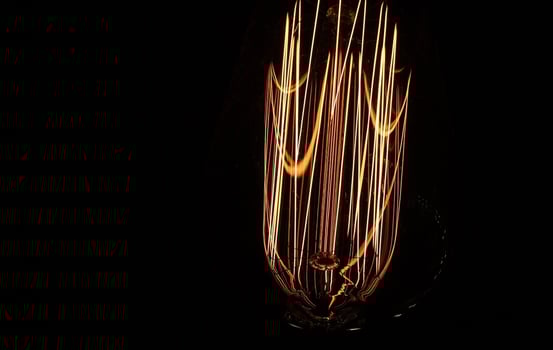 close up of retro light bulb on black background. Tungsten filaments glow with a warm orange light. The spiral vibrates with electricity. photo