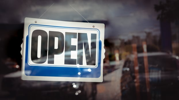 A black lettered store opening sign hangs on a glass door at a coffee shop with shadows of customers' cars parked for coffee. photo