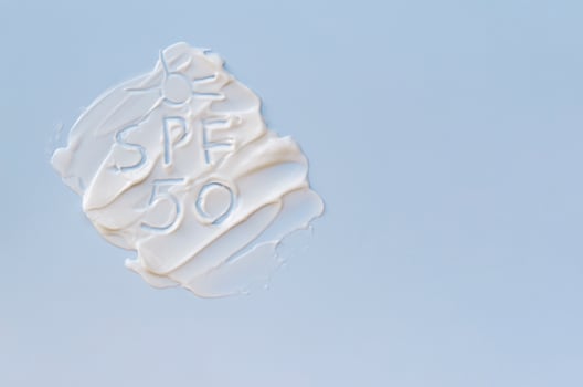 White cream texture on a blue background and SPF 50 text. The concept of skin protection, a banner with copy space. photo