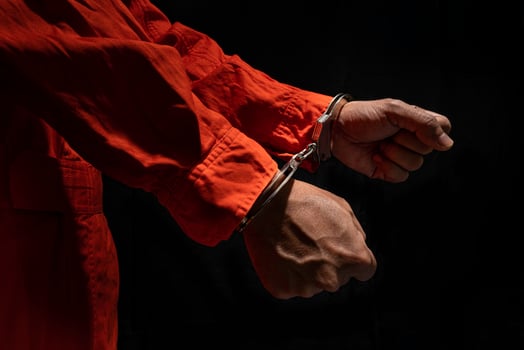 Handcuffs on Accused Criminal in Orange Jail Jumpsuit. Law Offender Sentenced to Serve Jail Time, in black background photo