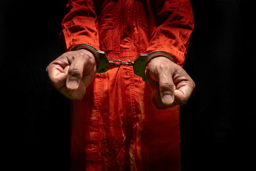 Handcuffs on Accused Criminal in Orange Jail Jumpsuit. Law Offender Sentenced to Serve Jail Time, in black background photo