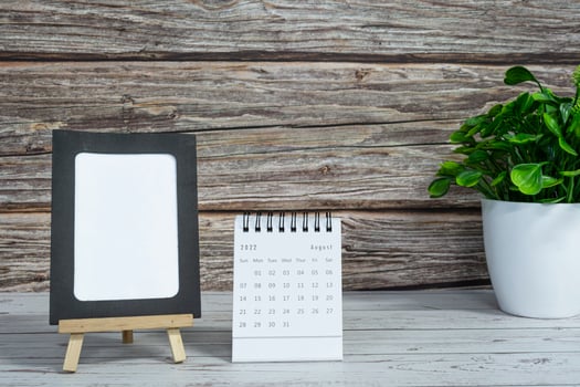 White August 2022 calendar on wooden desk with paper frame and potted plant. photo
