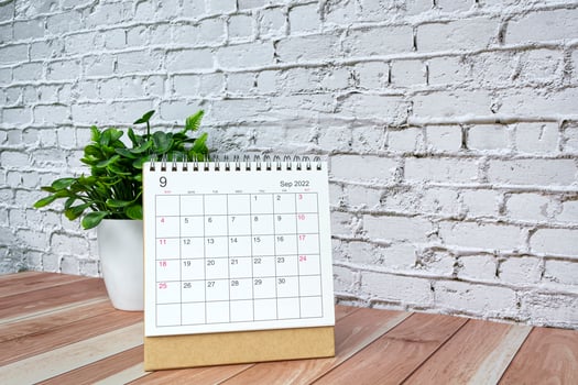 September 2022 white calendar with potted plant on wooden desk. photo