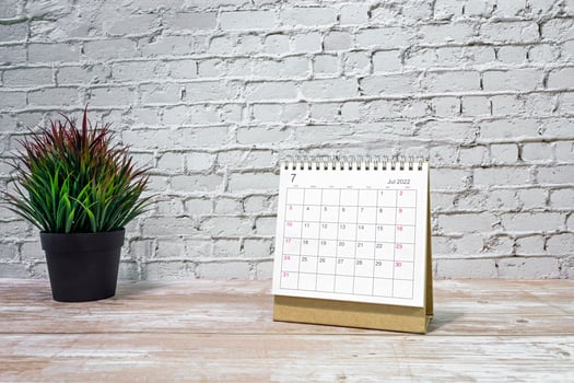 July 2022 white calendar with potted plant on wooden desk. photo