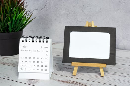 White October 2022 calendar on wooden desk with paper frame and potted plant. photo