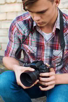 Photographer examining camera. Handsome young man examining his digital camera while sitting outdoors photo
