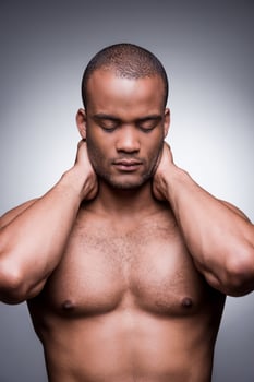 Dark and handsome. Young African man holding hands behind head and keeping eyes closed while standing against grey background photo