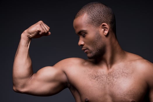 Proud of his perfect biceps.  Young shirtless African man looking at his biceps while standing against black background photo