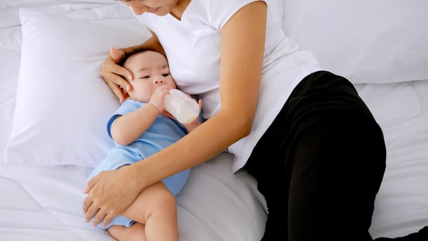 Young mother feeding little baby from milk bottle on bed. photo