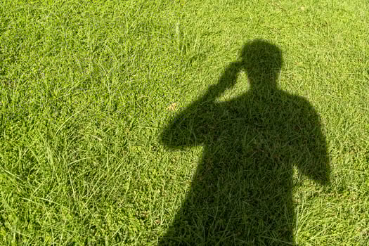 Shadow of a person using a phone on the grass photo