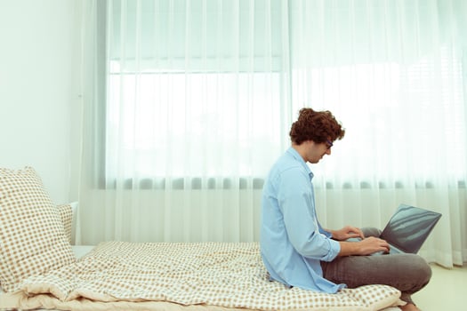 Young Caucasian Man work from home on laptop and connect online to office indoor for remote internet workplace. Young Adult male  is freelance work smart on notebook sitting on Bed bedroom, copy space photo
