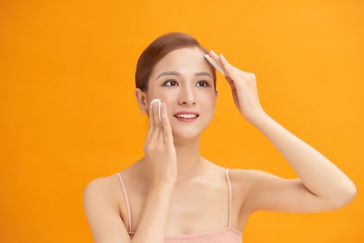 Beautiful young woman with silky skin using cotton pads on light background photo