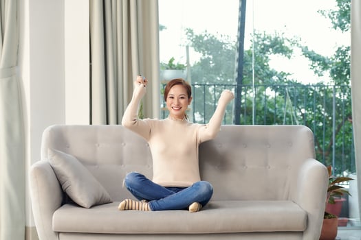 young woman looks winning sitting on the sofa with remote control in her hands watching sport game , cheer on her team at home photo