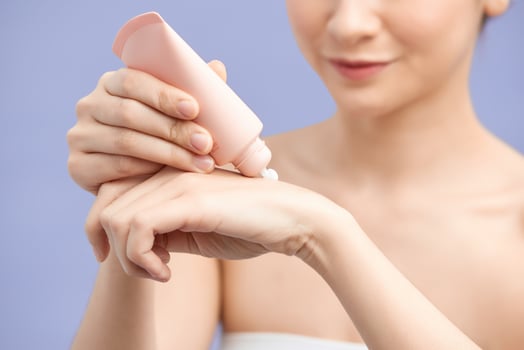 Happy woman hydrating hands skin with moisturizer cream on violet background photo