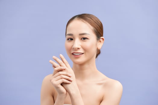 Smiling young woman applies cream on her hands. On a violetbackground. photo