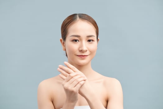 Portrait of happy smiling beautiful young woman touching skin or applying cream, isolated over violet background photo