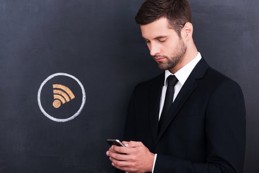 Wi-Fi zone. Handsome young man holding telephone while standing against sharing  symbol chalk drawing on blackboard photo