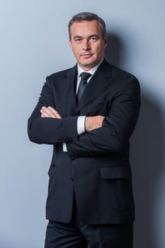 Confident business expert. Confident mature man in formalwear looking at camera and keeping arms crossed while standing against grey background photo