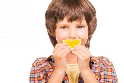 Having fun with orange. Cheerful little boy covering mouth with piece of orange while isolated on white photo